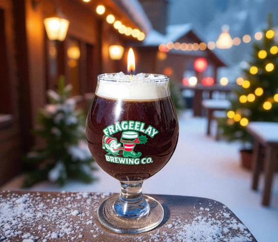 Glass of dark beer holiday beer candle with foam on a wooden table outdoors at night, featuring Frageelay Brewing Co. logo by CW Candle Co. Hand Poured in North Carolina 