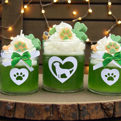 Three green jars dog themed candles with decorative elements on a wooden surface with string lights in the background.