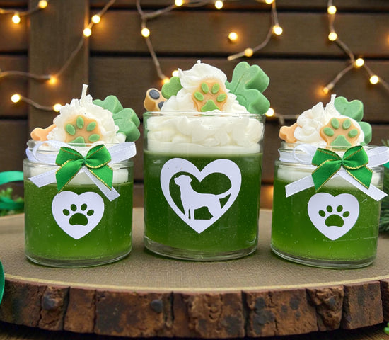 Three green jars dog themed candles with decorative elements on a wooden surface with string lights in the background.