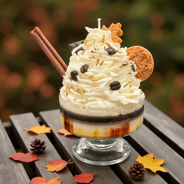  Decorative dessert candle with wax whip, cookie embeds, and a cinnamon  embed stick on a wooden surface with autumn leaves. Hand made by CW Candle Co. 