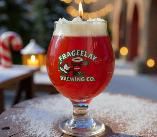 Red beer glass with white foam and a lit candle on top, featuring Frageelay Brewing Co. logo, outdoors with blurred lights and Christmas decorations.